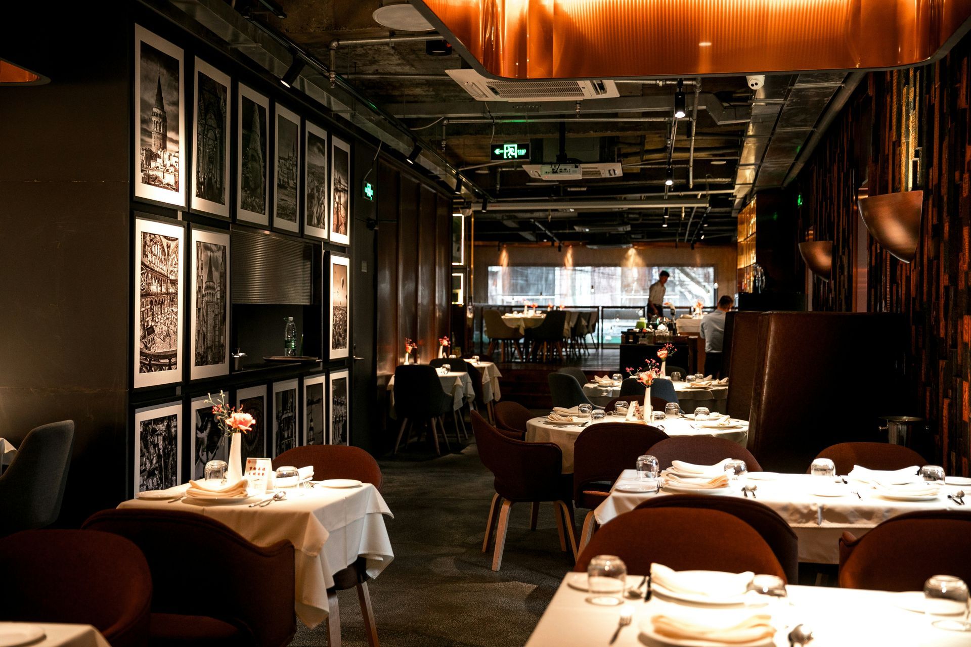 Interior of a restaurant with tables set for dining. Dark walls, art, warm lighting.