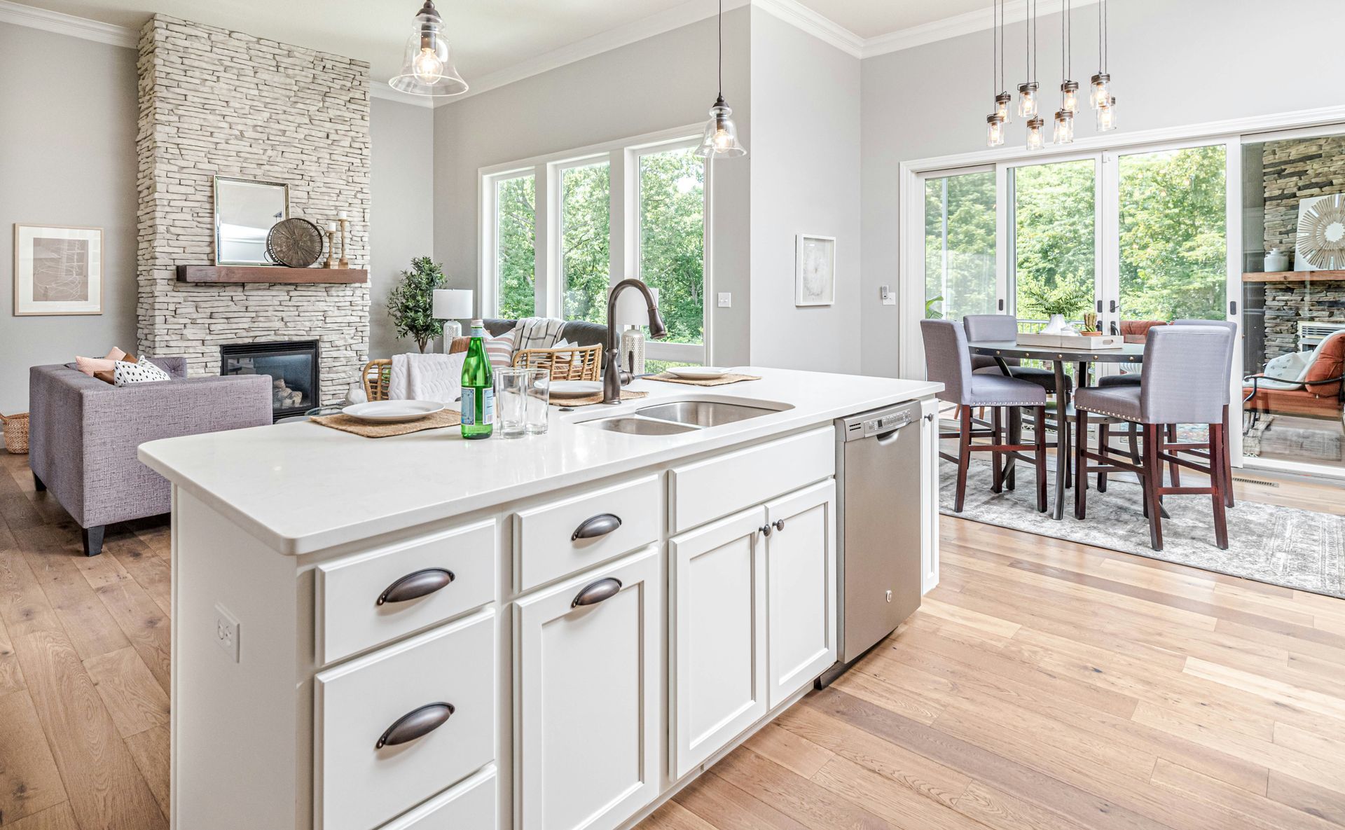 Open-concept kitchen and living area with a white island, dining table, and stone fireplace.