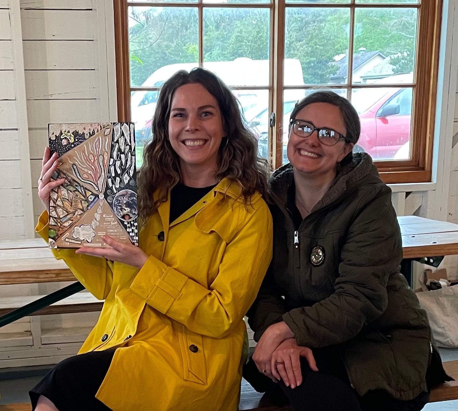 Two women are posing for a picture and one is holding a book