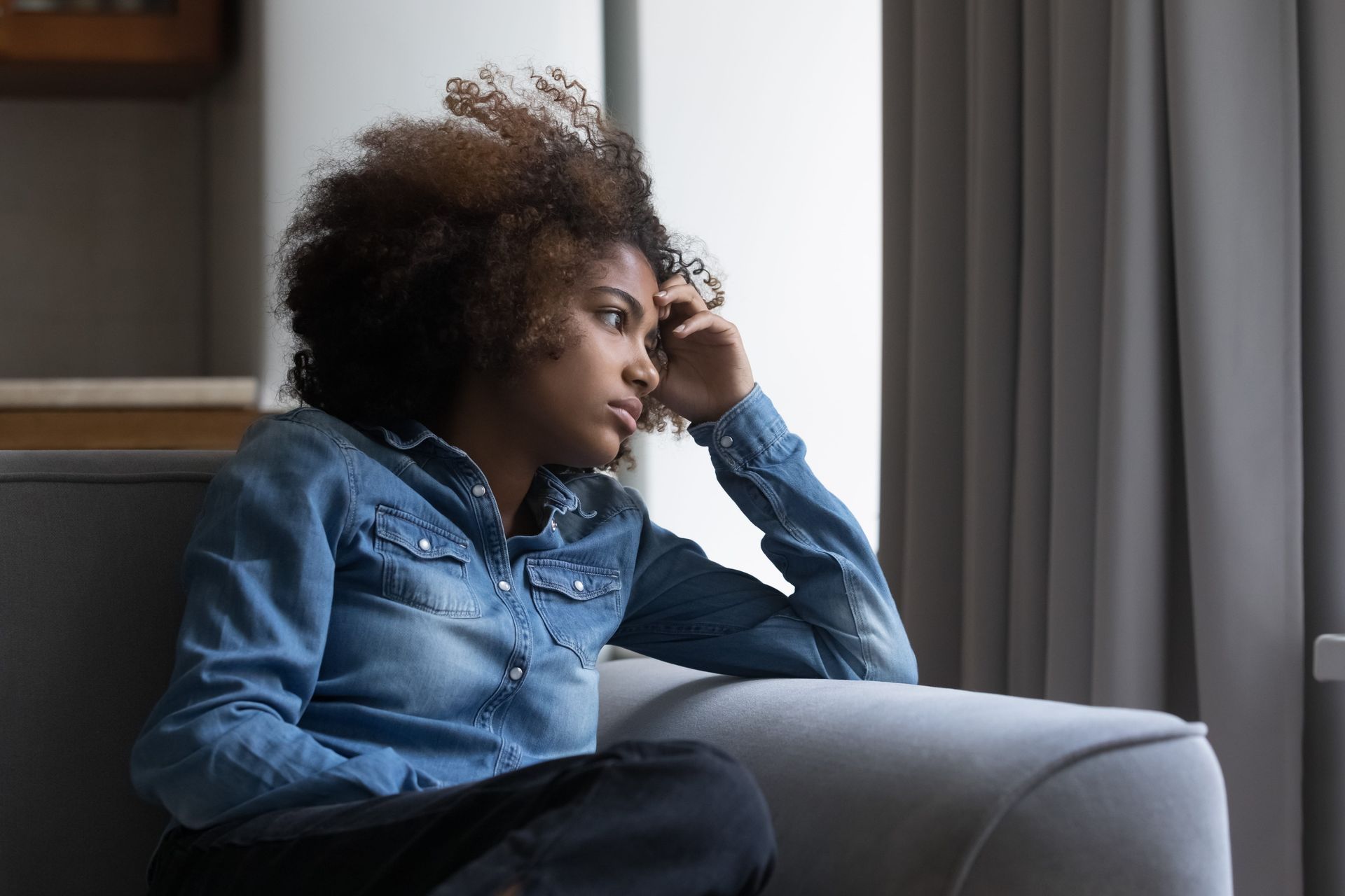 A young woman is sitting on a window sill looking out the window.