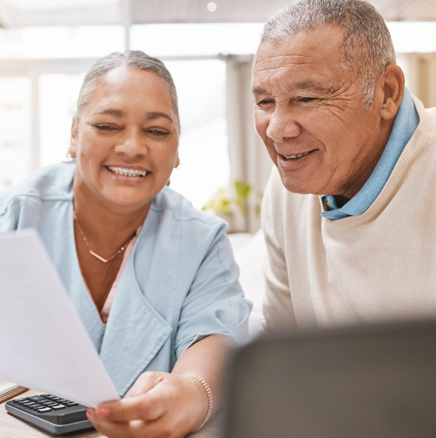 Two smiling people reviewing papers and using a calculator at a table with a laptop