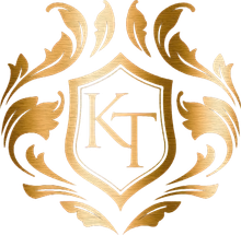 Gold ornamental monogram logo with “KT” inside a shield and laurel-like flourishes