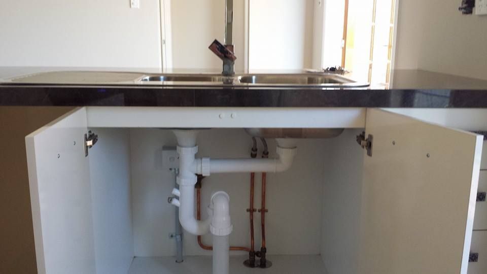 A plumber repairing pipes under a sink in a residential kitchen.