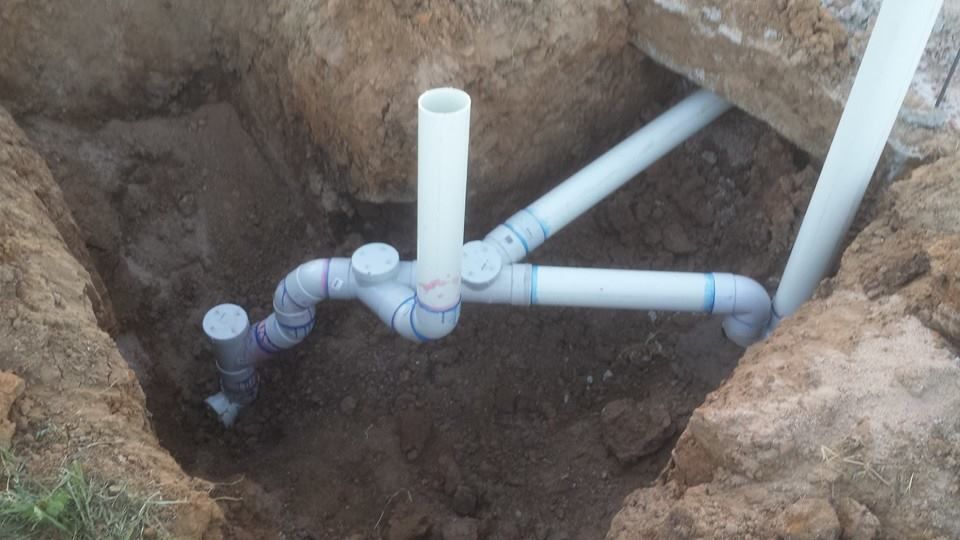 A bunch of pipes are laying in the dirt in a hole.