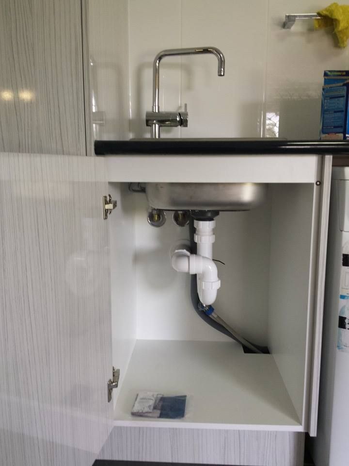 A plumber repairing pipes under a sink in a residential kitchen.