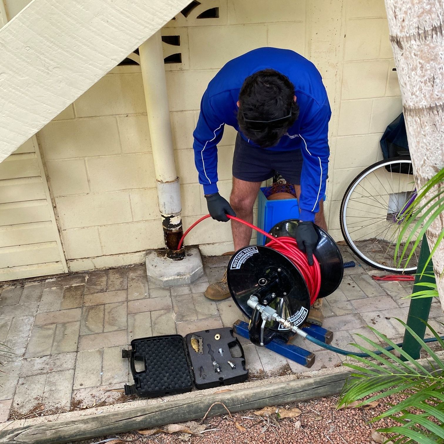Plumber using a drain cleaning tool to clear a blocked pipe outside a building