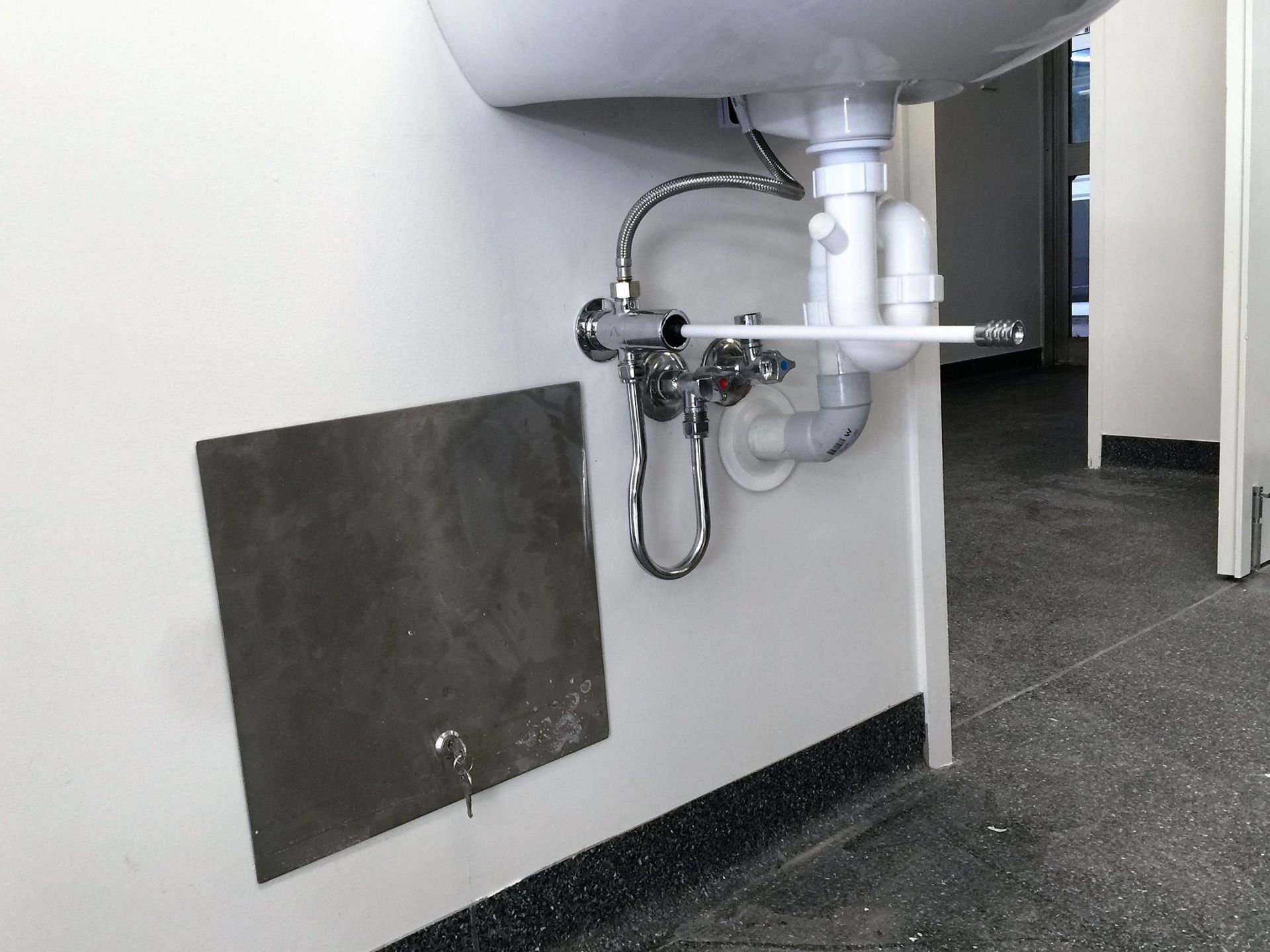 Plumbing installation under a sink with access panel and connections visible