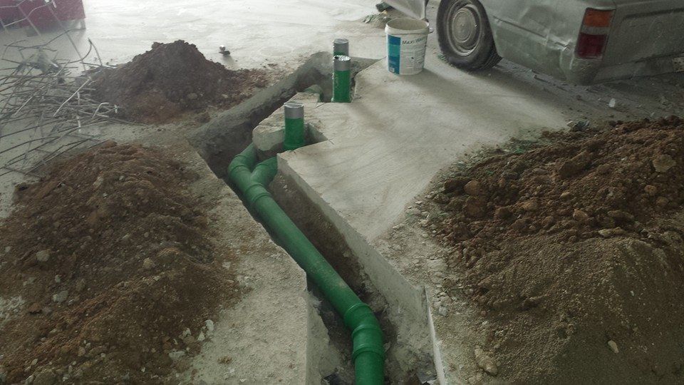 A green pipe is being installed in a hole in the ground.