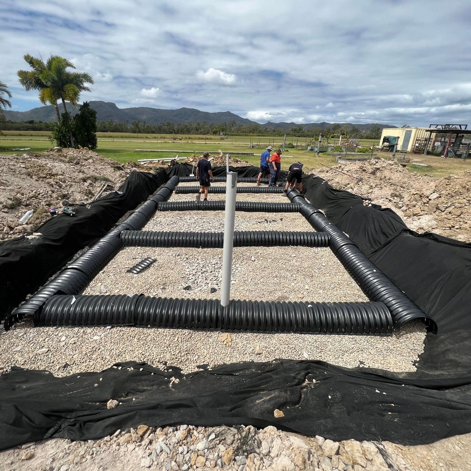 Workers installing black drainage pipes in a trench at a construction site