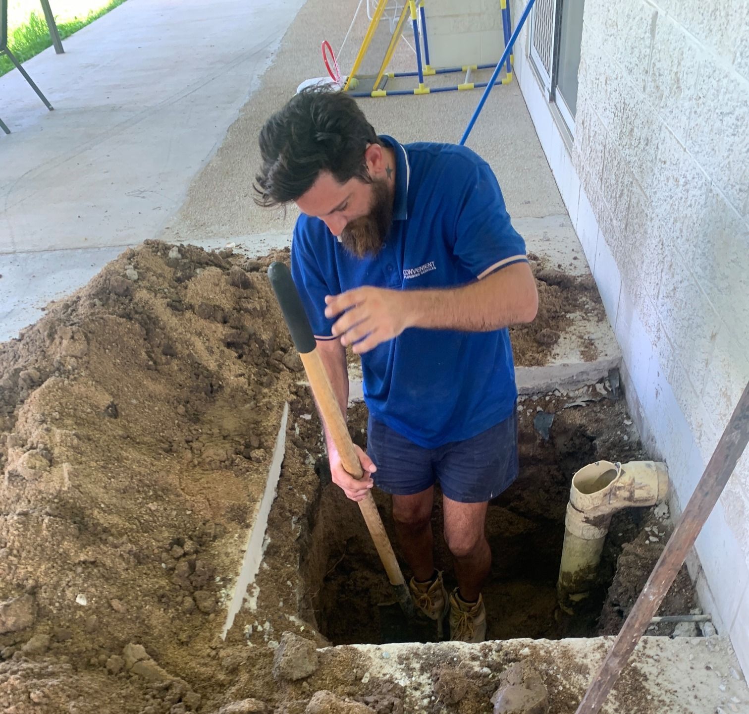 Plumber digging a trench for drainage installation outside a building