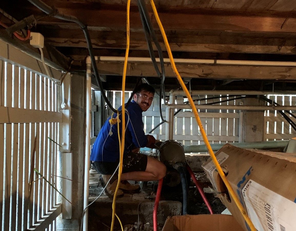 Plumber working under a house, using equipment to clear pipes