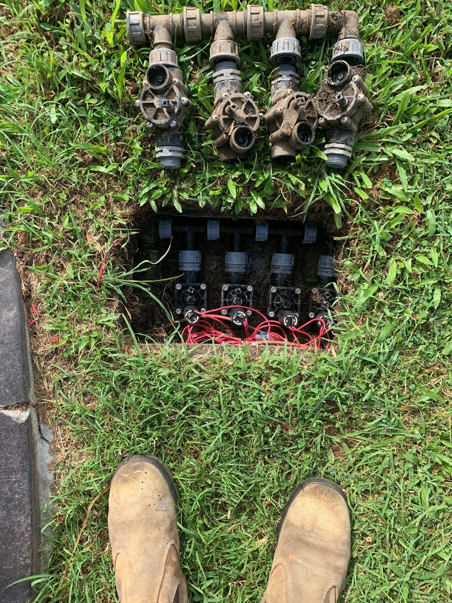 A person is standing in front of a sprinkler system in the grass.