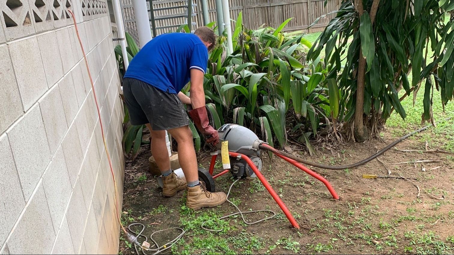 Plumber using a drain cleaning machine to clear a pipe in a yard