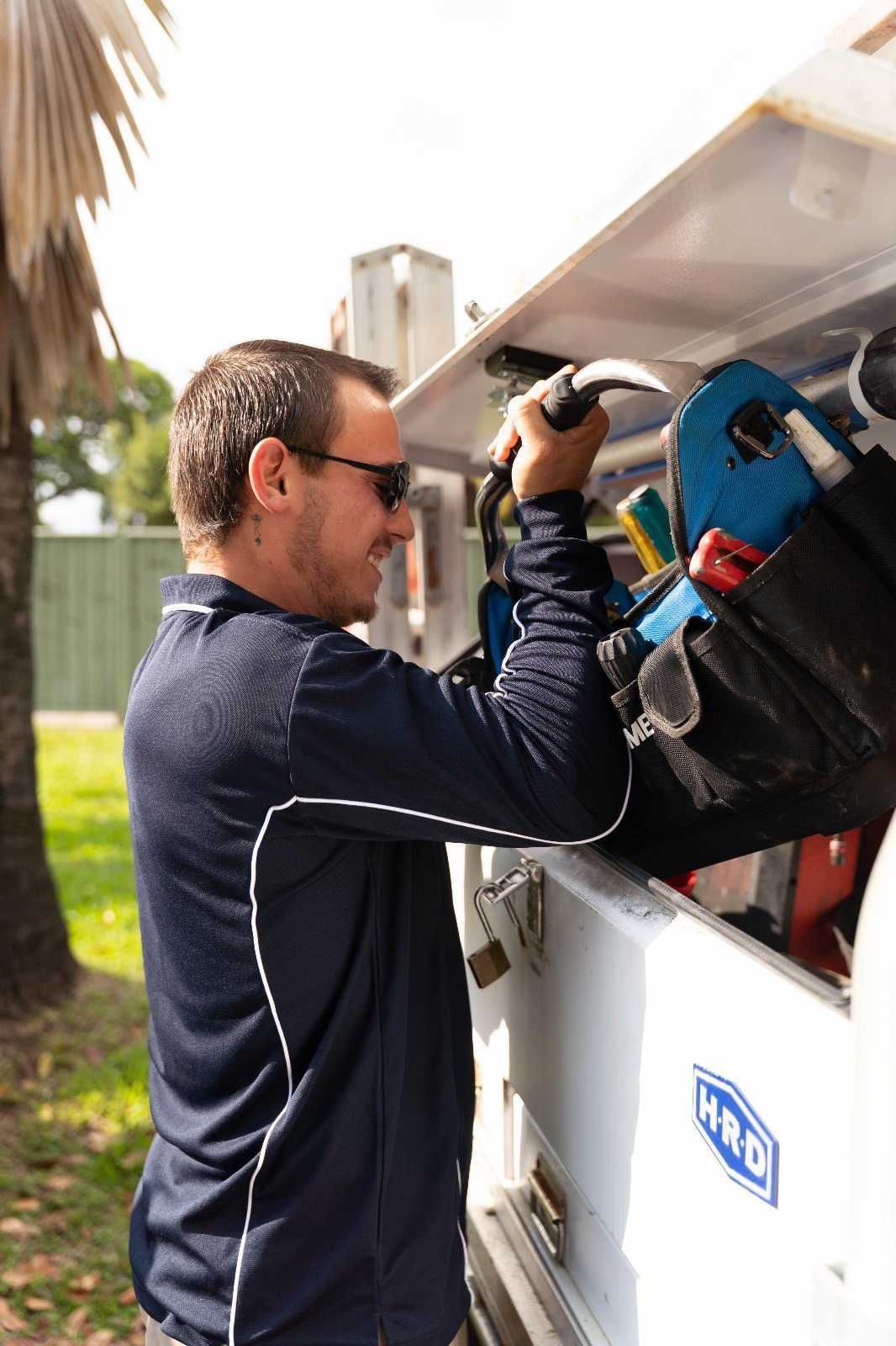 A man in a blue shirt is standing under a house holding a hose.