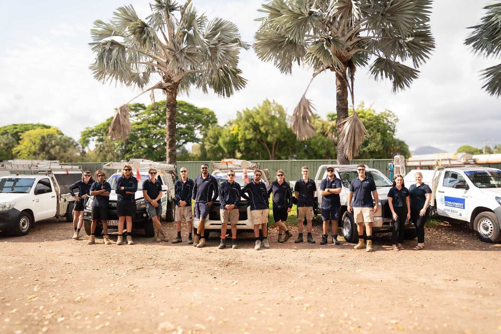 Group of workers standing with work trucks outdoors near palm trees.