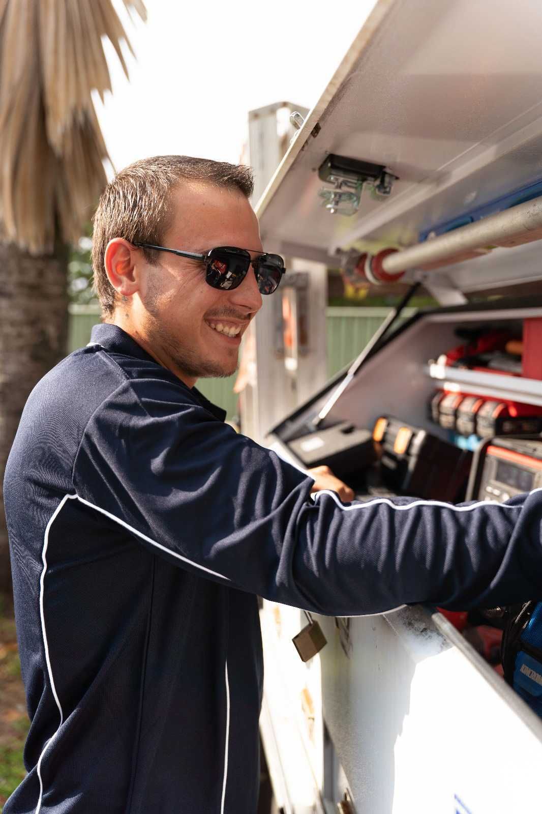 Man in sunglasses smiles while looking in a white toolbox in an outdoor setting.