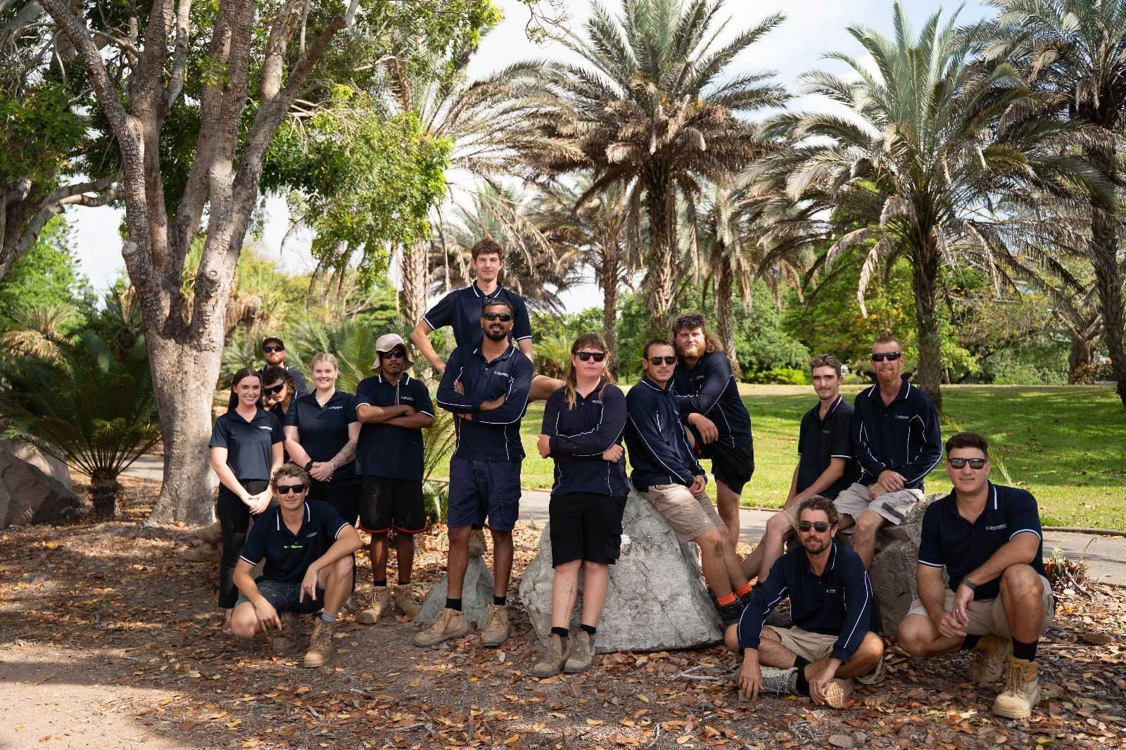 Group of people in navy shirts and shorts posing outdoors near trees and rocks.