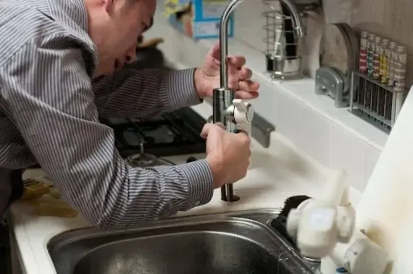 Man fixing a kitchen sink faucet, leaning over the sink, holding a wrench.