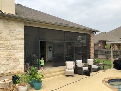 Patio with outdoor seating beside a screened porch, with a child standing near the doorway.