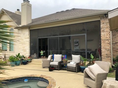 Patio with wicker chairs and potted plants beside a screened-in backyard seating area and small pool