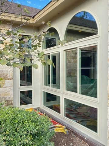 White-framed arched windows and glass doors on a house exterior beside green shrubs and stone siding