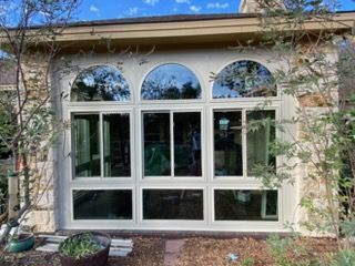 Large cream-colored house window with three arched panes and surrounding greenery