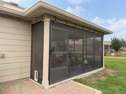 Screened patio enclosure attached to a beige house with large mesh windows and a grassy yard