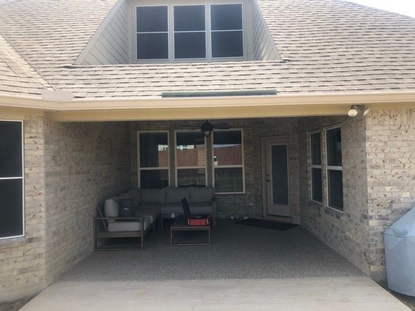 A brick house has a covered patio with a couch and chairs