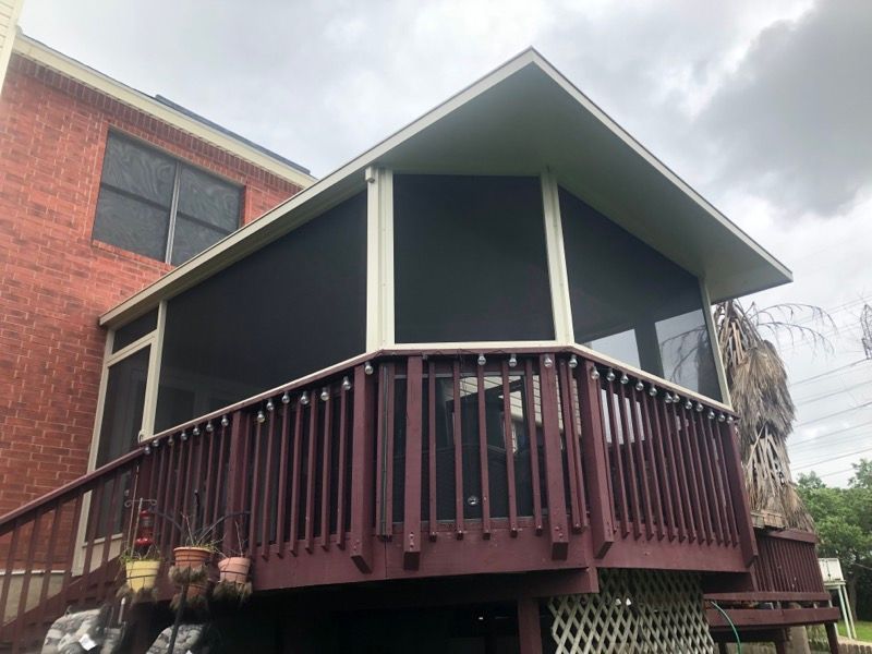 A screened in porch with a red deck next to a brick house.