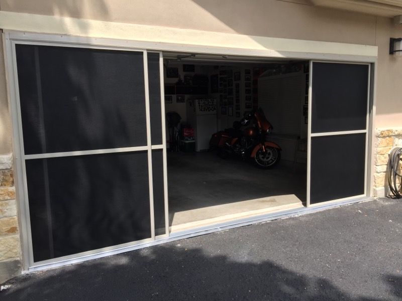 A motorcycle is parked in a garage with a screen door.