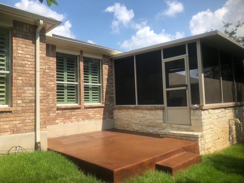 A screened in porch with a wooden deck in front of a brick house.