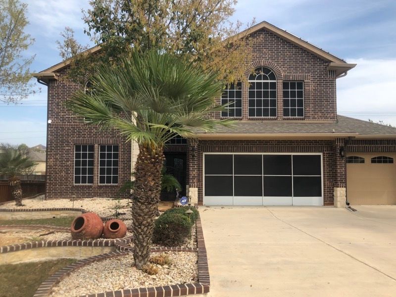 A large brick house with a screened in garage and a palm tree in front of it.