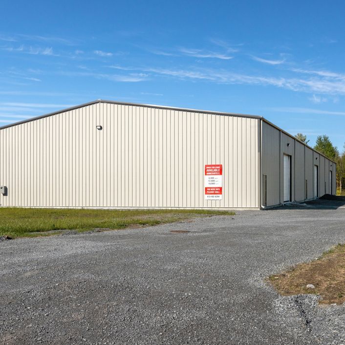 White metal warehouse on a gravel lot under a blue sky, with red signs on the side.