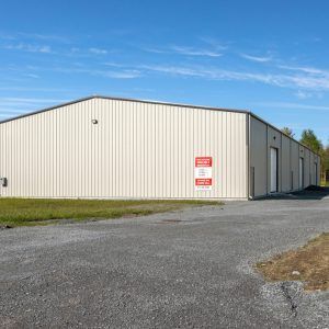 Large white metal warehouse beside a gravel lot under a clear blue sky
