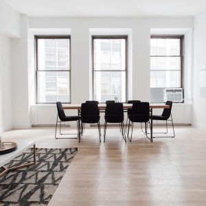 Bright minimalist dining room with black chairs, a wooden table, and three tall windows.