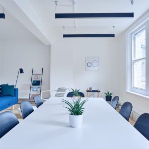 Bright minimalist conference room with long white table, blue chairs, and large windows