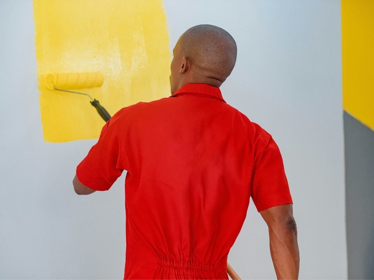 Person in a red shirt painting a yellow wall with a roller