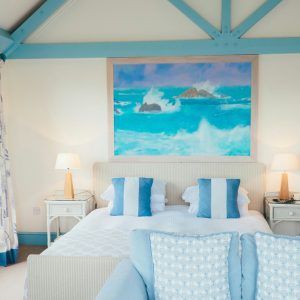 Bright beach-themed bedroom with twin beds, blue accents, lamps, and ocean painting