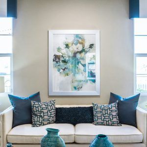 Bright living room with a cream sofa, teal pillows, abstract art, and blue vases in front of windows