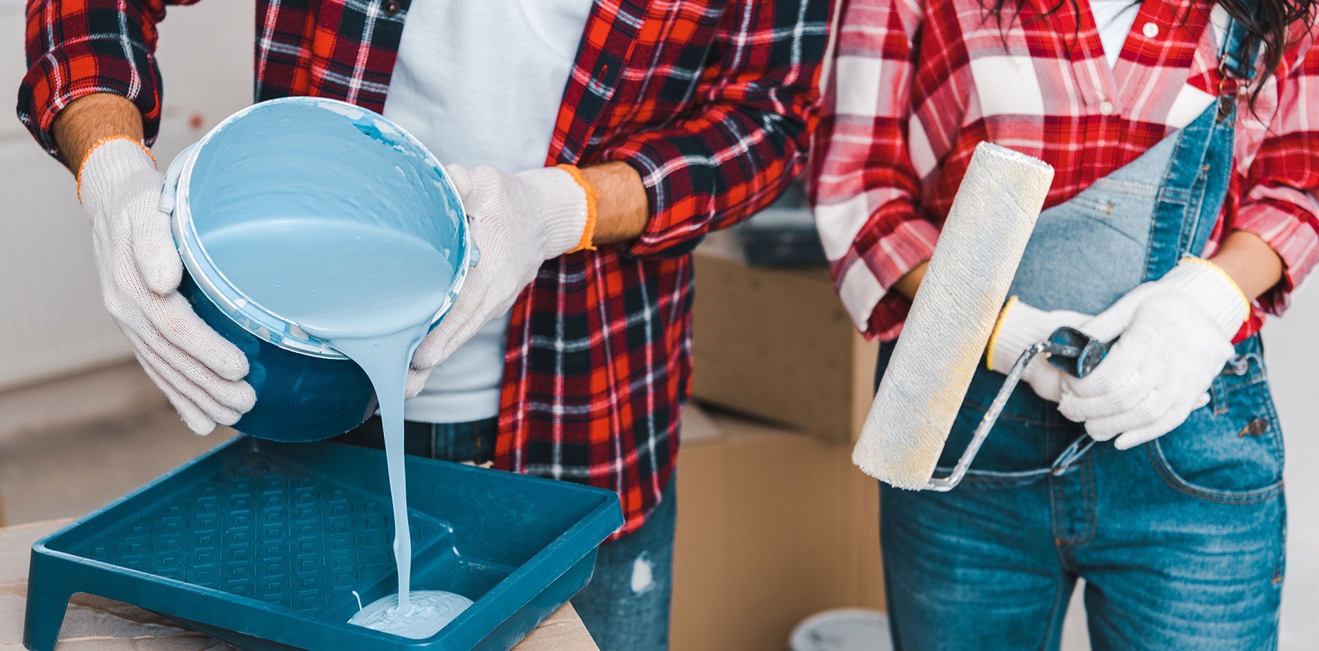 Two people in plaid shirts painting a blue tray and wall with roller and bucket
