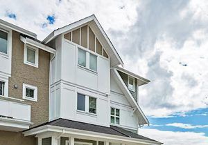 White multi-story house with gray trim and pitched roof under a cloudy blue sky