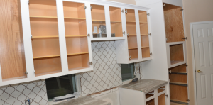 White kitchen with open cabinets, tiled backsplash, sink, and a door on the right.