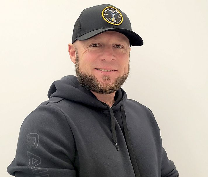Man in a black cap and hoodie smiling against a plain light background