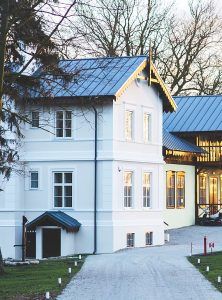 White house with blue roof and lit windows beside a paved driveway at dusk