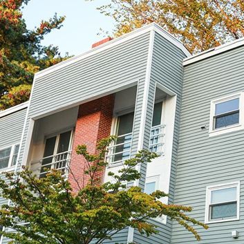 Modern apartment building with light gray siding, red brick accents, and trees in front