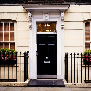Black front door with white trim and black iron fence on a cream townhouse facade