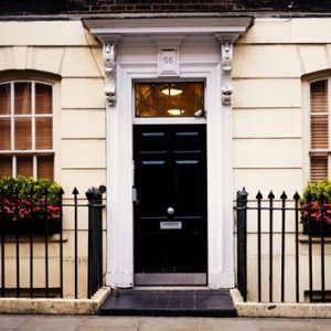 Black front door with white trim and iron railings on a cream townhouse facade.
