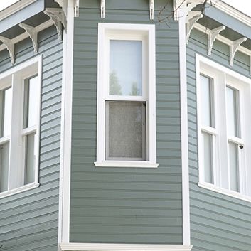 Gray house exterior with white-trimmed bay windows and decorative eaves