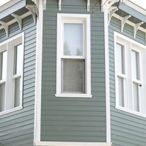 Close-up of a green house exterior with white trim and tall windows on a corner bay facade