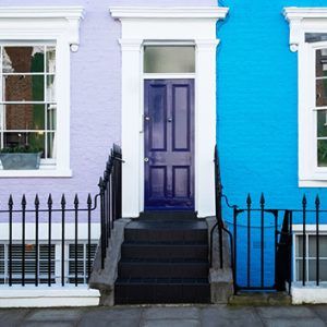 Pastel rowhouse entrance with a purple door, black steps, and bright blue and lavender walls